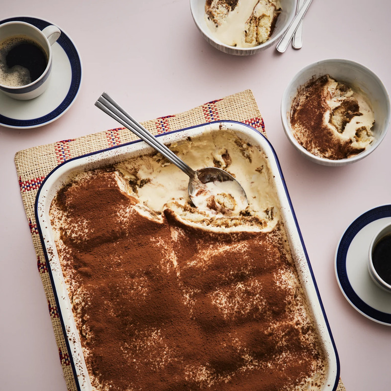 Halva tiramisu i form pudrad med kakao, med synliga lager av kräm och kaffedoppade savoiardikakor.