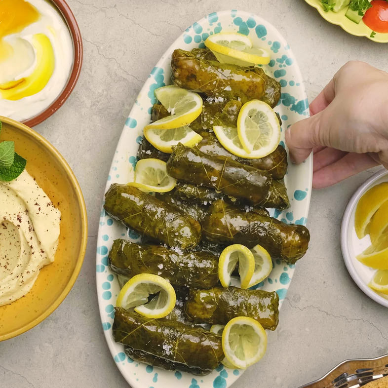 Närbild på hemgjorda vinbladsdolmar fyllda med ris, pinjenötter och aromatiska kryddor, snyggt upplagda på ett fat. Serverade med citron och en lätt glans av olivolja, perfekta som en del av en meze-buffé eller mellanösterninspirerad måltid.