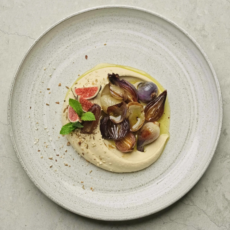 Hummus toppad med rostad dukkah, karamelliserad lök, fikon och olivoljestekta dadlar på ett stort serveringsfat