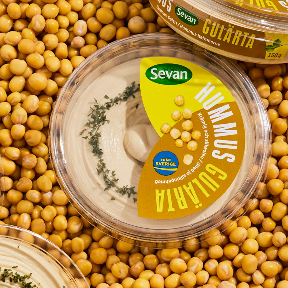 A container of hummus surrounded by yellow peas.