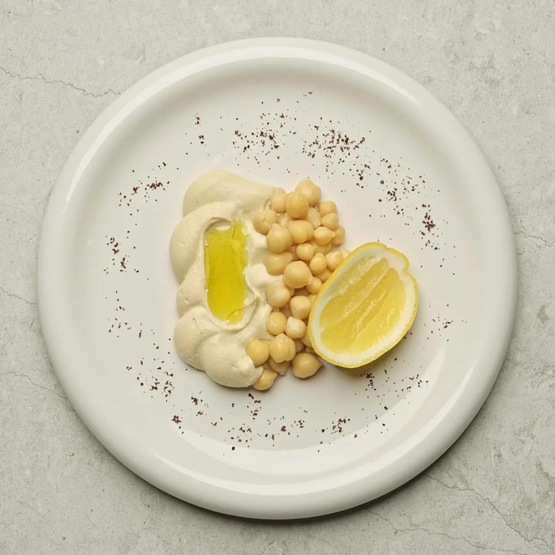 Krämig hummus med hela kokta kikärtor, olivolja, citron och röd sumac serverad på ett fat