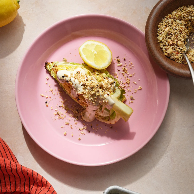 Grillad spetskål toppad med tahinisås och dukkah på en tallrik med citronklyfta.